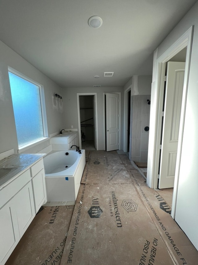 bathroom with a garden tub, a tile shower, visible vents, and vanity