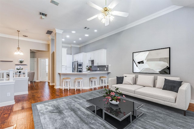 living room featuring ceiling fan with notable chandelier, decorative columns, ornamental molding, and dark hardwood / wood-style floors