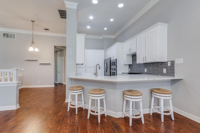 kitchen with stainless steel appliances, crown molding, kitchen peninsula, dark hardwood / wood-style flooring, and white cabinets