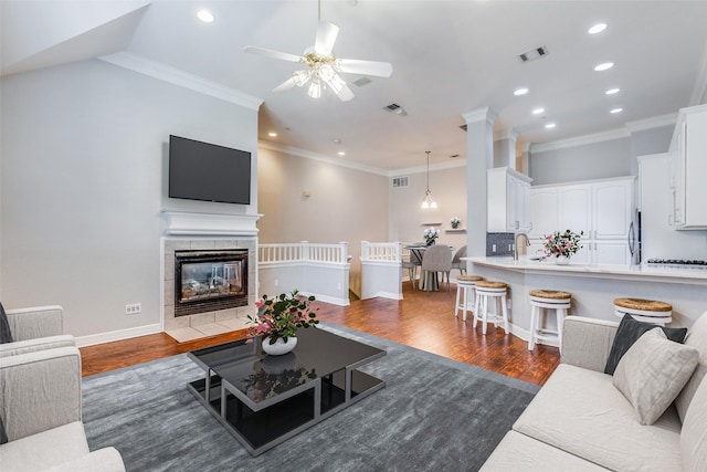 living room with a tile fireplace, ceiling fan, crown molding, and dark hardwood / wood-style flooring