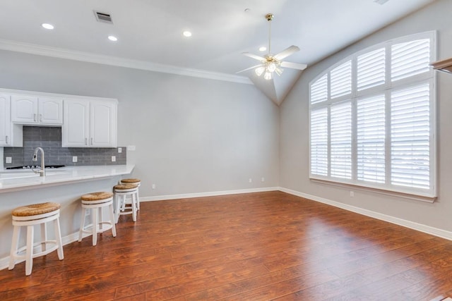 kitchen featuring ceiling fan, a breakfast bar, lofted ceiling, white cabinetry, and backsplash