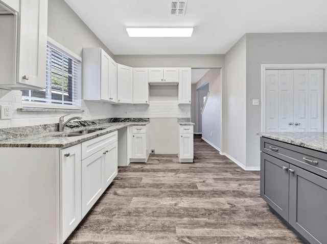 kitchen featuring white cabinetry, sink, light stone countertops, and hardwood / wood-style flooring