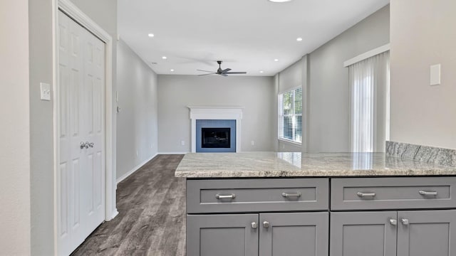 kitchen with light stone countertops, dark hardwood / wood-style flooring, ceiling fan, and gray cabinetry