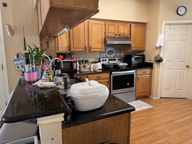 kitchen with light wood-type flooring, dark stone counters, stainless steel range with electric cooktop, and sink