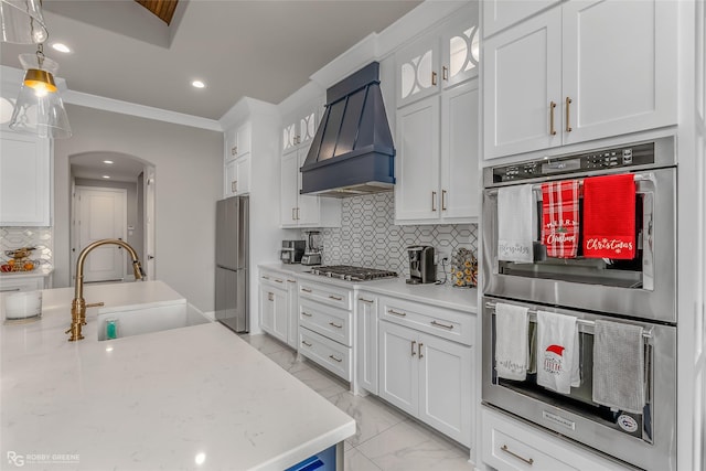 kitchen with white cabinetry, sink, backsplash, stainless steel appliances, and custom range hood