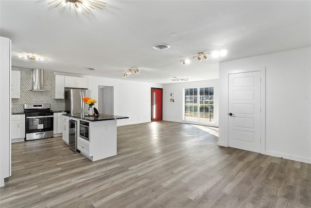 kitchen with appliances with stainless steel finishes, backsplash, a kitchen island, wall chimney range hood, and white cabinetry