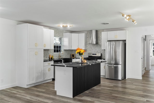 kitchen featuring wall chimney range hood, appliances with stainless steel finishes, tasteful backsplash, a kitchen island, and white cabinetry