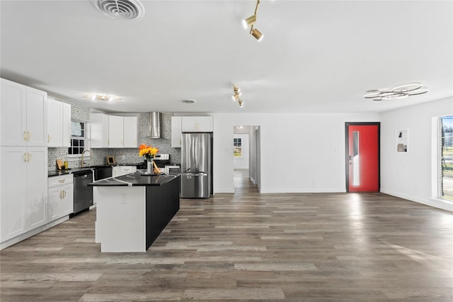 kitchen with wall chimney range hood, a kitchen island, decorative backsplash, white cabinets, and appliances with stainless steel finishes