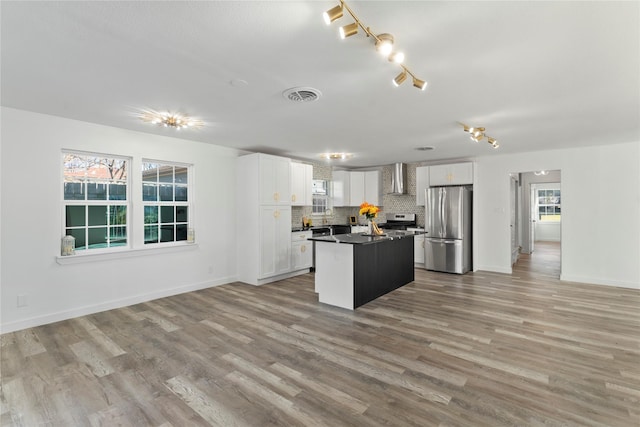 kitchen with white cabinets, wall chimney range hood, decorative backsplash, appliances with stainless steel finishes, and a kitchen island