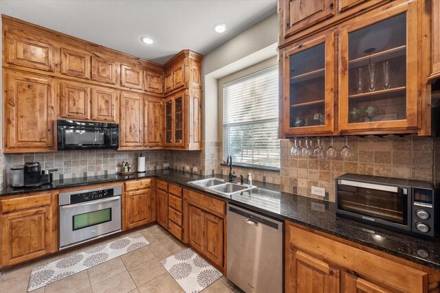 kitchen featuring sink, dark stone counters, decorative backsplash, light tile patterned floors, and black appliances