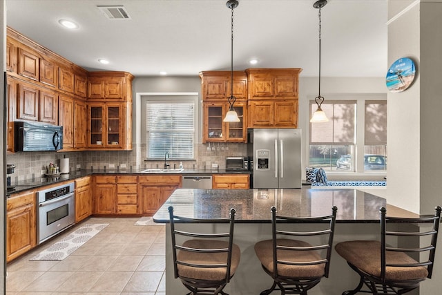 kitchen with hanging light fixtures, dark stone countertops, decorative backsplash, a breakfast bar, and black appliances