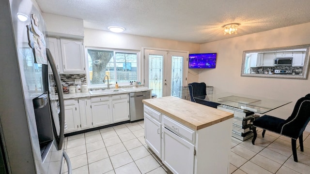 kitchen featuring sink, light tile patterned floors, appliances with stainless steel finishes, tasteful backsplash, and white cabinets