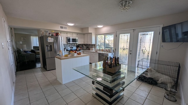 kitchen with light tile patterned flooring, appliances with stainless steel finishes, white cabinetry, sink, and french doors