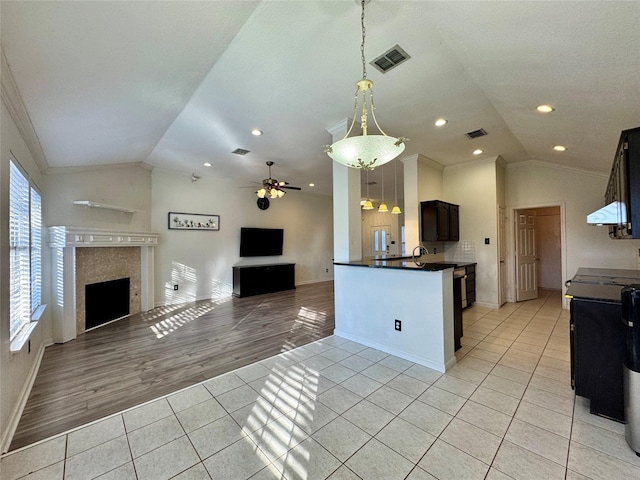 kitchen with light tile patterned floors, ceiling fan, crown molding, and a tiled fireplace