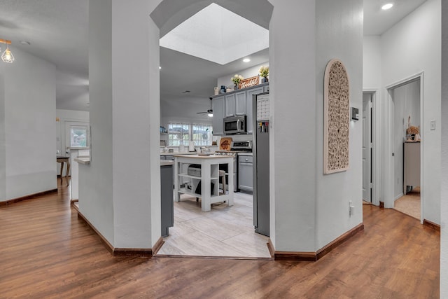 hall featuring light wood-type flooring, baseboards, arched walkways, and recessed lighting