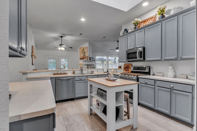 kitchen featuring gray cabinetry, stainless steel appliances, a peninsula, a sink, and tasteful backsplash