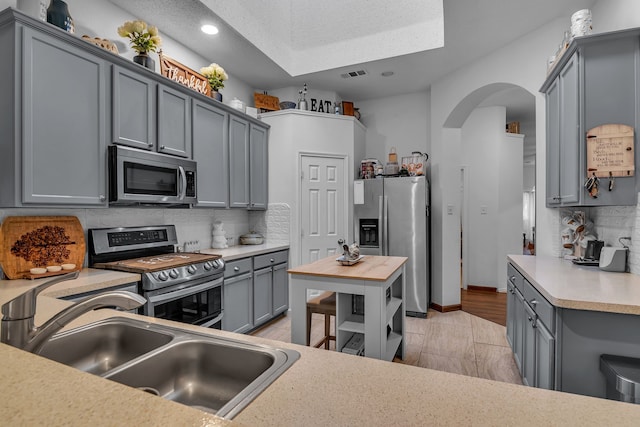 kitchen with gray cabinets, decorative backsplash, stainless steel appliances, and a sink