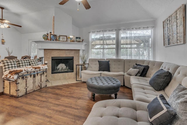 living area featuring lofted ceiling, a tiled fireplace, a ceiling fan, and wood finished floors