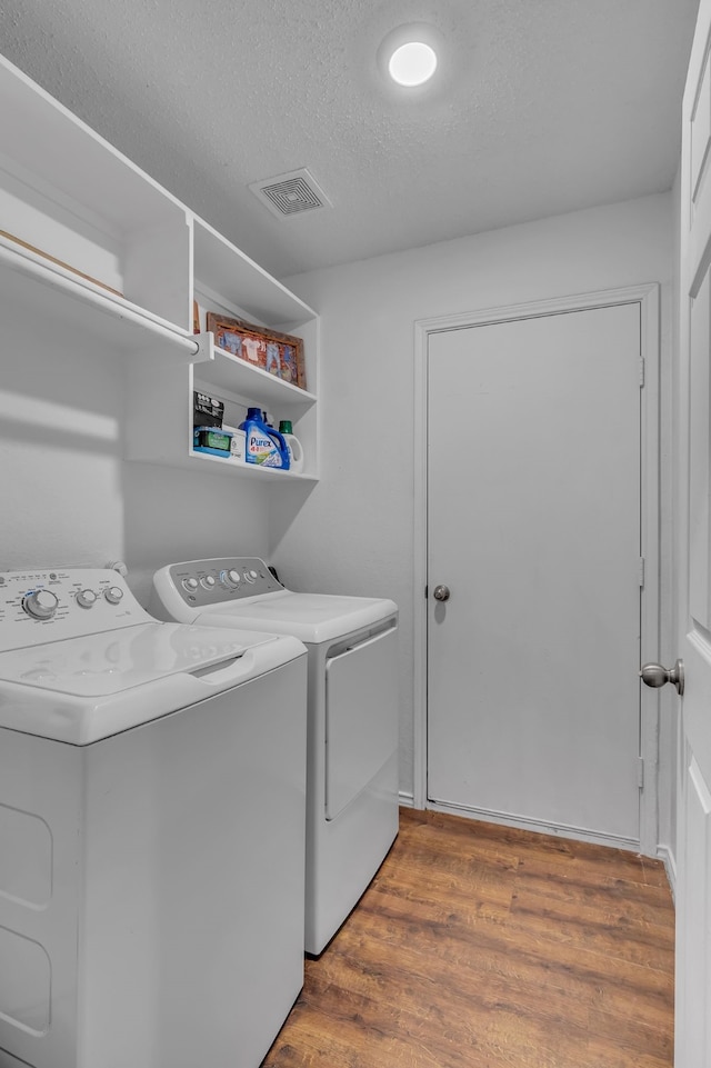 laundry area featuring washer and clothes dryer, visible vents, a textured ceiling, wood finished floors, and laundry area