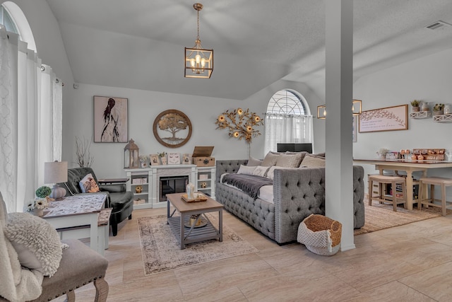 living area featuring a glass covered fireplace, visible vents, vaulted ceiling, and a notable chandelier