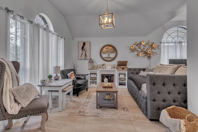 living room with a chandelier, a healthy amount of sunlight, a fireplace, and vaulted ceiling