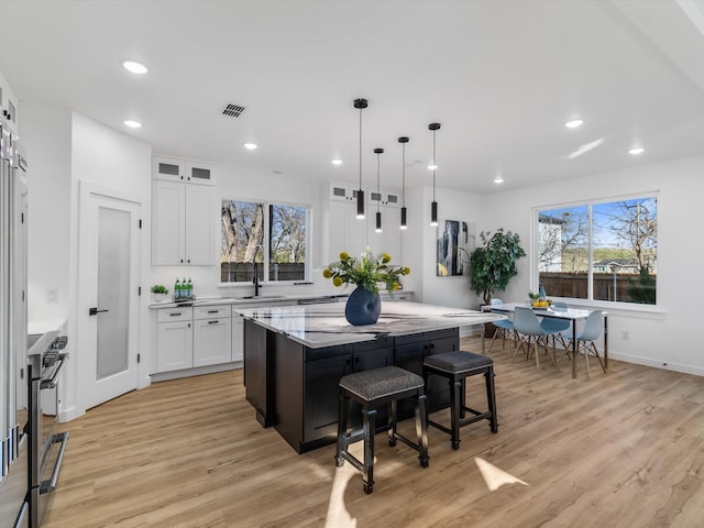 kitchen featuring a kitchen island, a kitchen bar, white cabinetry, stainless steel range, and light stone counters