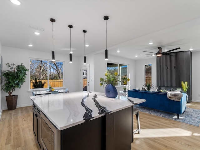 kitchen with hanging light fixtures, light wood-type flooring, built in microwave, and light stone counters