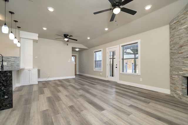 unfurnished living room featuring baseboards, lofted ceiling, wood finished floors, a fireplace, and recessed lighting