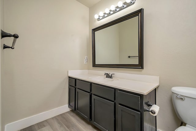 bathroom with toilet, wood finished floors, vanity, and baseboards