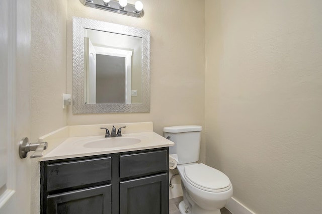 half bath featuring toilet, a textured wall, and vanity