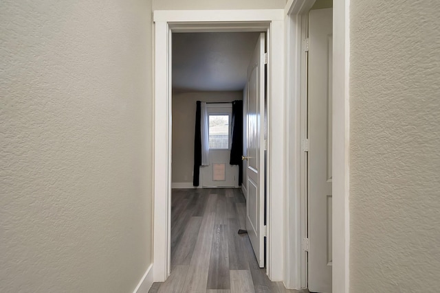 hallway featuring a textured wall, light wood finished floors, and baseboards