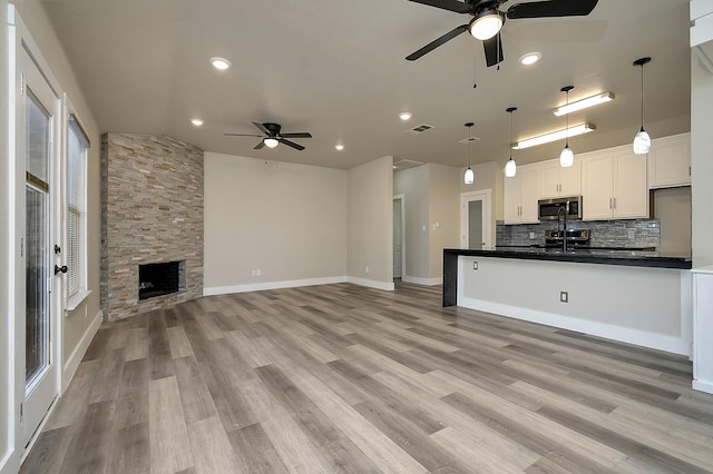 unfurnished living room with a fireplace, visible vents, light wood-style floors, ceiling fan, and baseboards