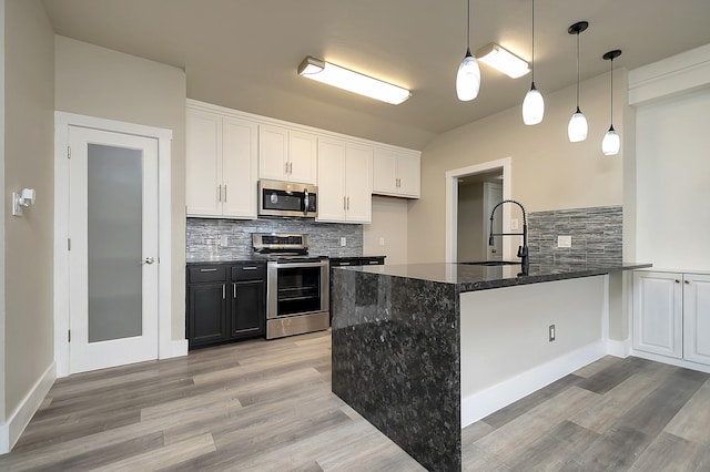 kitchen featuring a sink, dark stone counters, appliances with stainless steel finishes, a peninsula, and white cabinets