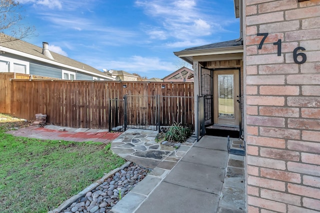 property entrance featuring a gate, brick siding, fence, and roof with shingles