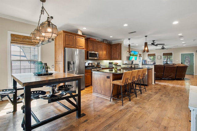 kitchen with appliances with stainless steel finishes, a breakfast bar, ceiling fan with notable chandelier, light hardwood / wood-style floors, and hanging light fixtures