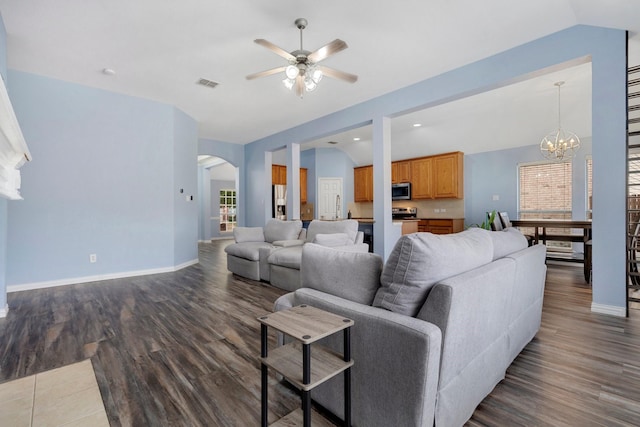 living room with ceiling fan with notable chandelier, dark hardwood / wood-style flooring, and vaulted ceiling