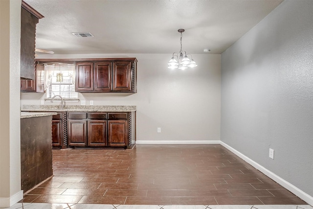 kitchen featuring dark brown cabinetry, sink, decorative light fixtures, and a notable chandelier