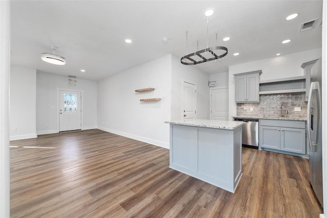 kitchen featuring gray cabinetry, dark hardwood / wood-style floors, backsplash, a kitchen island, and appliances with stainless steel finishes