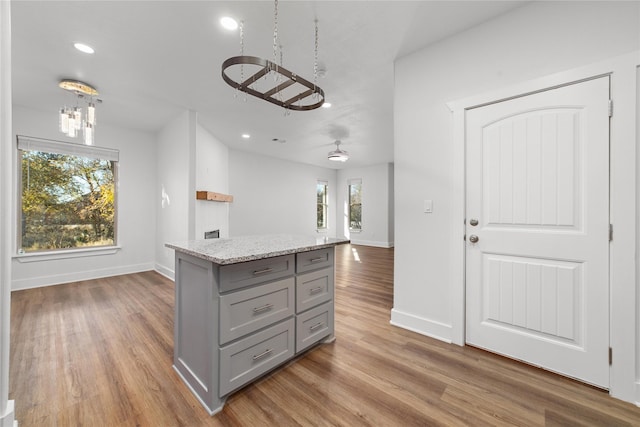 kitchen with a center island, gray cabinets, light stone countertops, and wood-type flooring