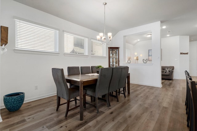 dining room with hardwood / wood-style floors, vaulted ceiling, and an inviting chandelier