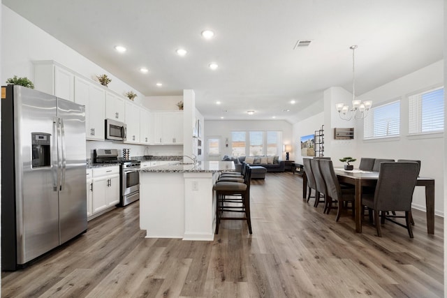 kitchen featuring stone counters, white cabinetry, hanging light fixtures, and appliances with stainless steel finishes