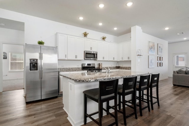 kitchen with light stone countertops, appliances with stainless steel finishes, white cabinetry, a breakfast bar area, and an island with sink