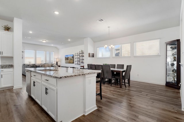 kitchen with light stone counters, sink, pendant lighting, a center island with sink, and white cabinetry