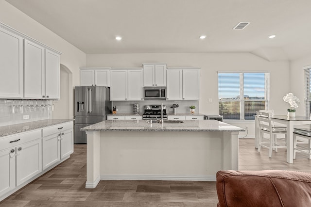 kitchen featuring a center island with sink, white cabinets, light stone countertops, and stainless steel appliances