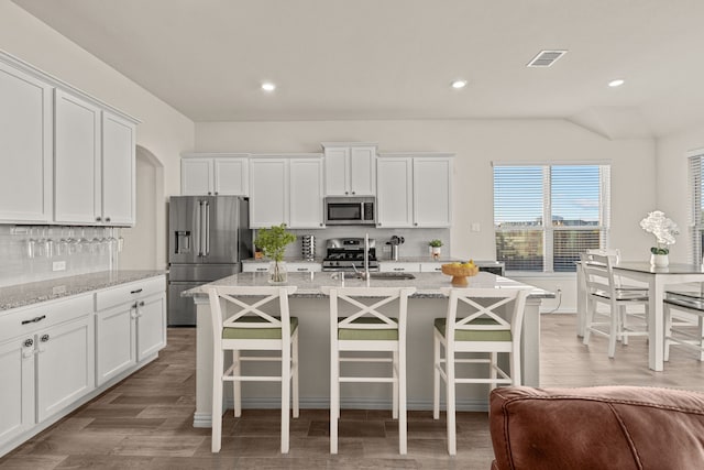 kitchen with light stone countertops, stainless steel appliances, and an island with sink