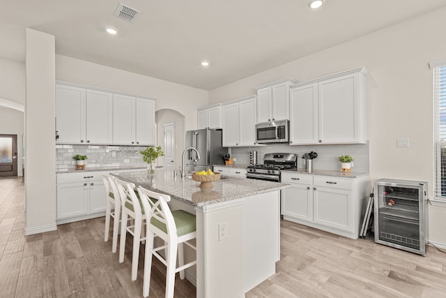 kitchen with light wood-type flooring, stainless steel appliances, white cabinetry, and an island with sink