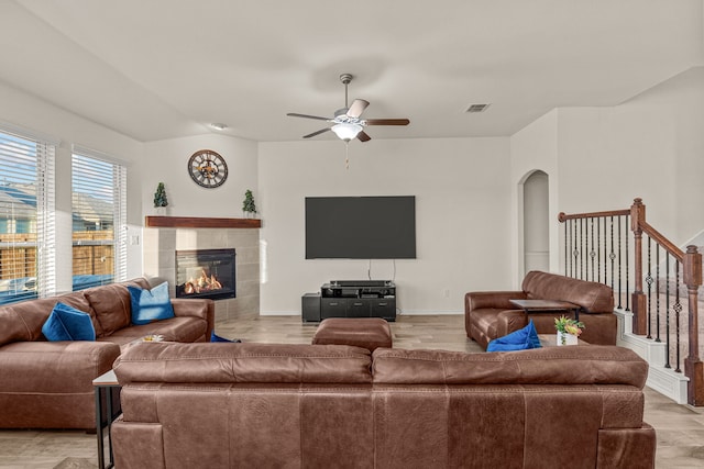 living room with a tiled fireplace, ceiling fan, light hardwood / wood-style flooring, and vaulted ceiling