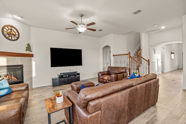 living room featuring a tiled fireplace, ceiling fan, and light wood-type flooring