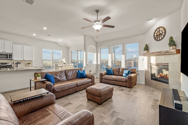 living room featuring a fireplace, light hardwood / wood-style floors, vaulted ceiling, and ceiling fan