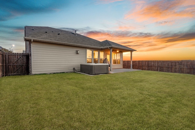 back house at dusk featuring a yard, cooling unit, a patio, and a hot tub